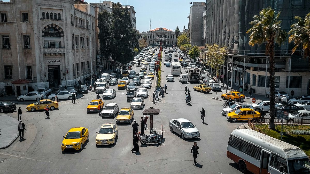 شارع مزدحم بالسيارات في وسط دمشق، ومحطة الحجاز في نهايته.